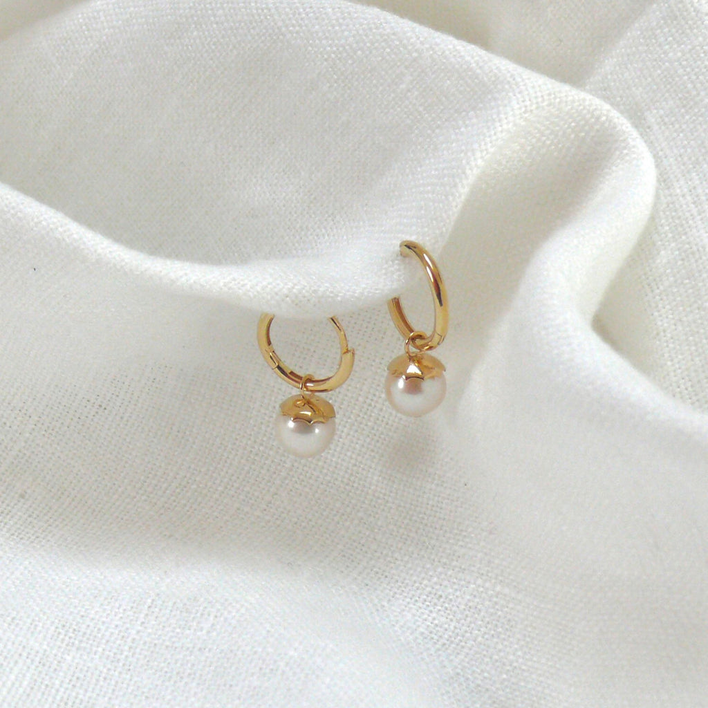 9ct gold huggies earrings with pearls on a white linen fabric. The earrings are by Misia Mae