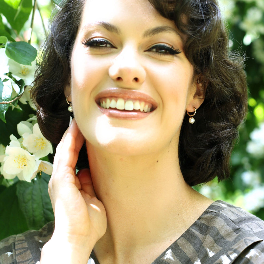 A dark haired woman smiling wearing 9ct gold huggies earrings with pearls by Misia Mae