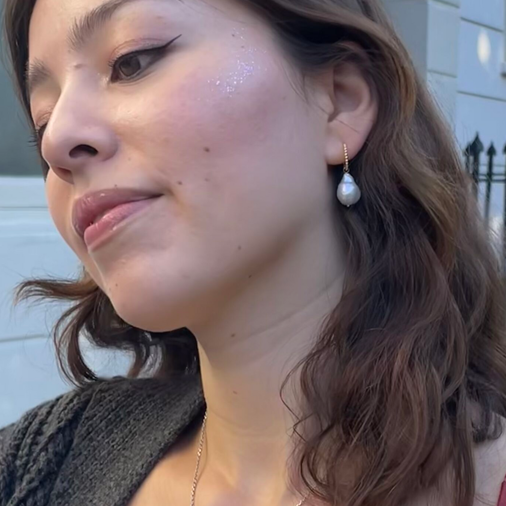 A dark haired woman wearing baroque pearl gold earrings by Misia Mae