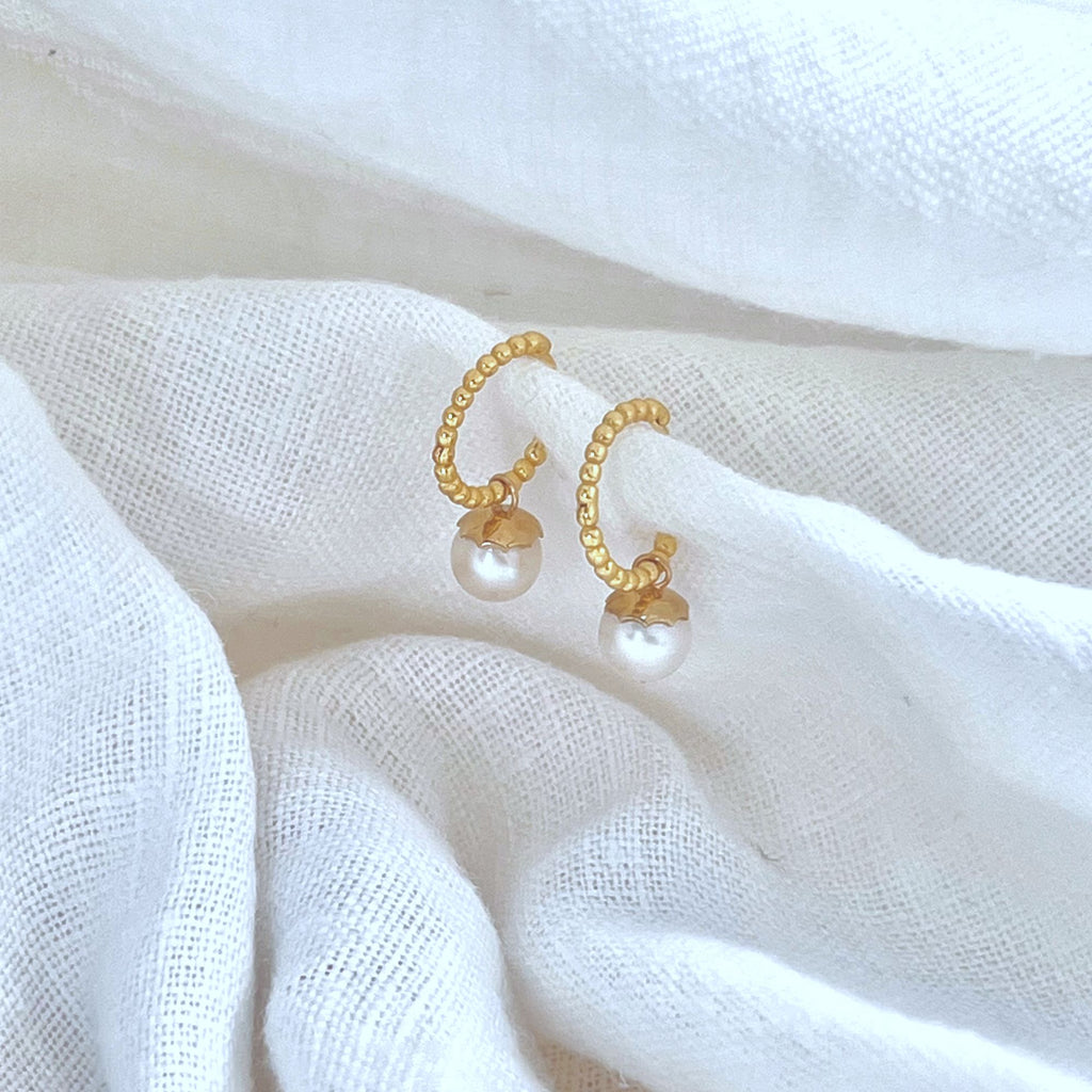 Beaded gold huggie hoop earrings with pearls on white linen background