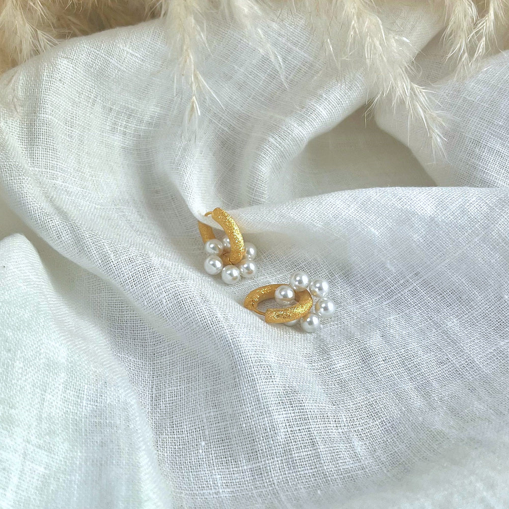 Chunky gold earrings with pearl charms on a white linen background