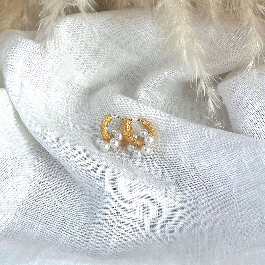 Chunky gold earrings with faux white pearl circle charms by Misia Mae on a white linen background