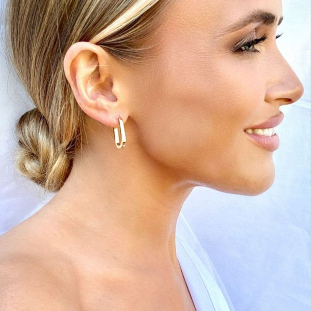 A blonde woman wearing gold rectangle earrings from the Zoe collection by Misia Mae