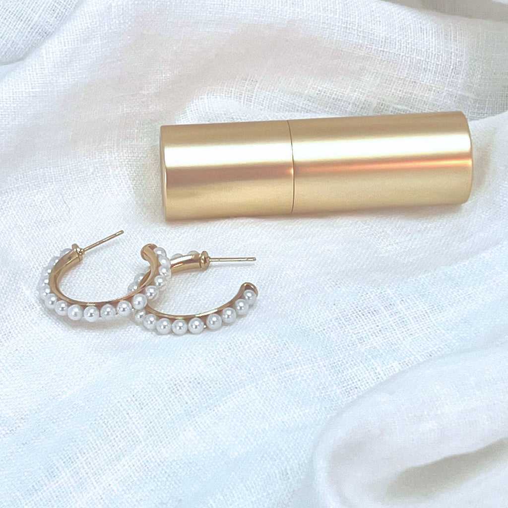 Pearl hoop earrings and a lipstick on a white linen fabric. Earrings by Misia Mae