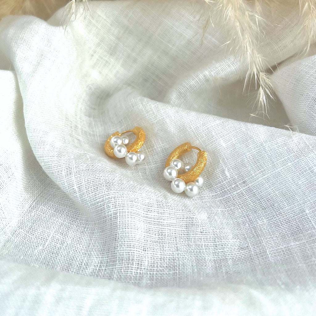 Chunky gold earrings with faux white pearl circle charms by Misia Mae on a white linen background