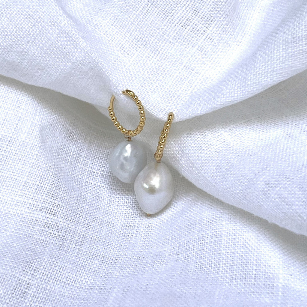 baroque pearl beaded gold huggies earringson a white linen background. Earrings by Misia Mae