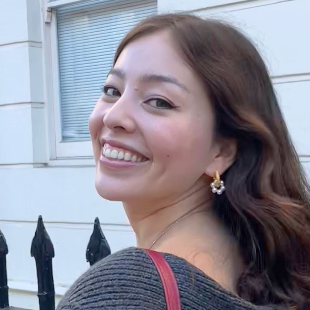 A dark haired woman wearing chunky gold hoop earrings with pearl charms by Misia Mae