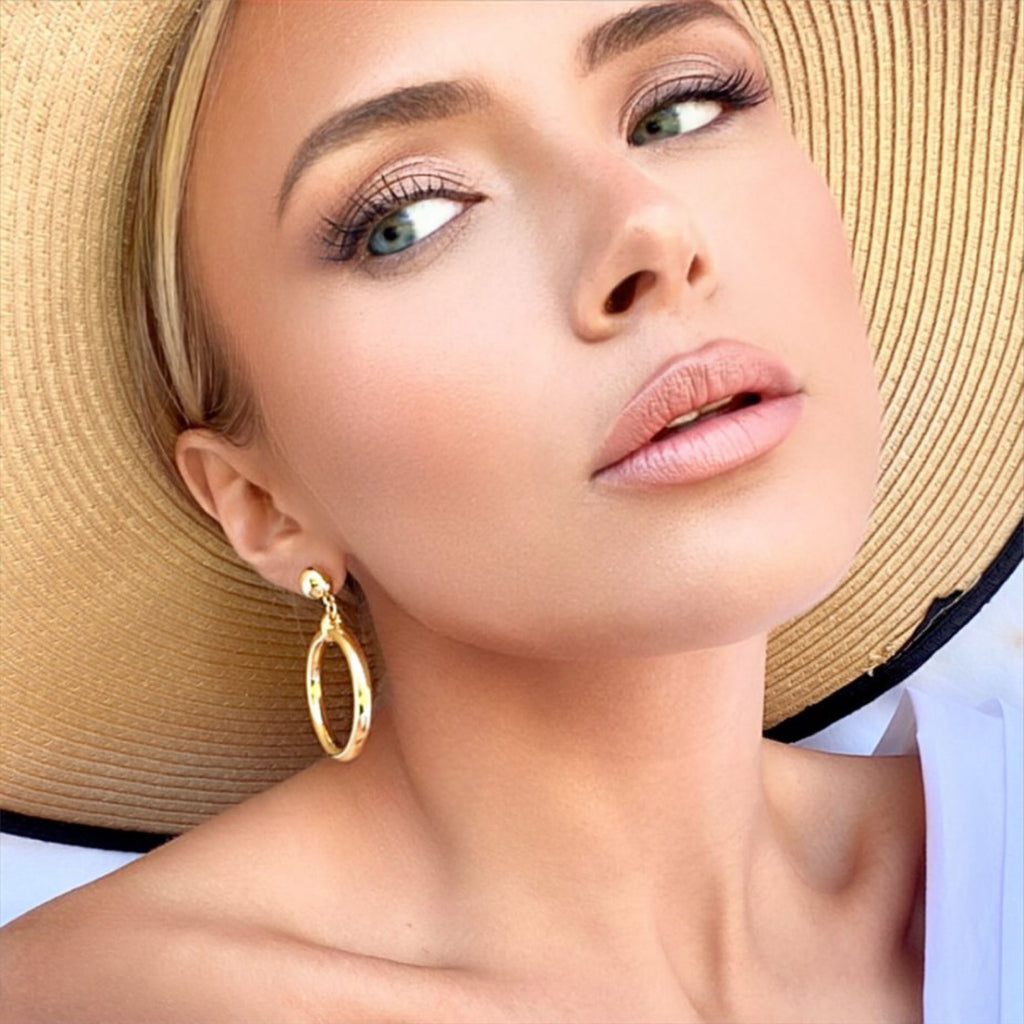 A blond woman wearing a straw hat and chunky gold hoop earrings by Misia Mae