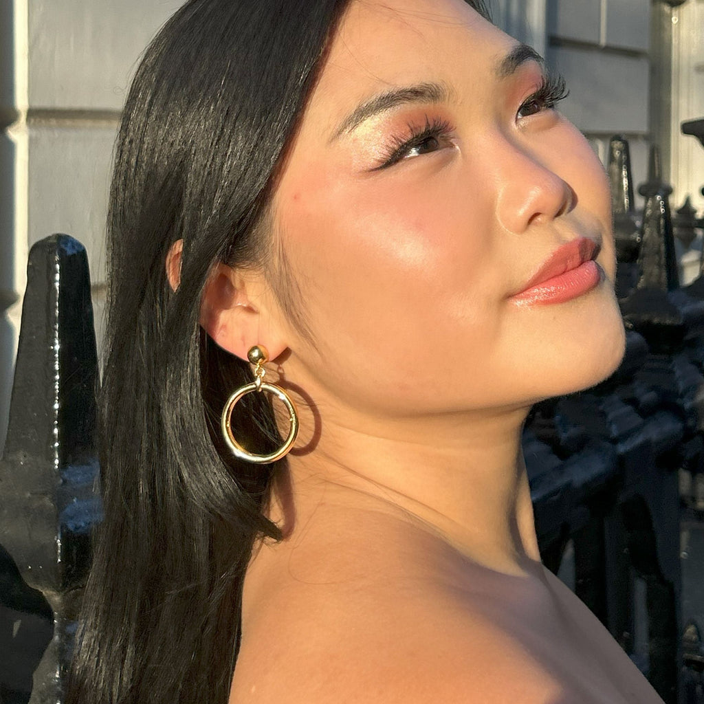 A dark haired Asian woman wearing a prom dress and chunky gold hoop earrings from the Audrey collection by Misia Mae