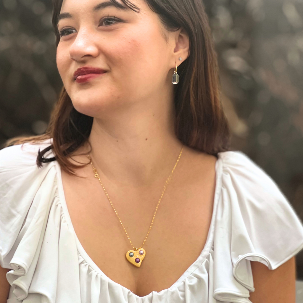 a brunette woman in a white shirt wearing gold heart necklace with three pearls by Misia Mae