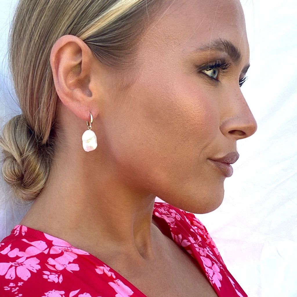 A blonde woman wearing a hot pink dress with flowers and gold huggie earrings with baroque pearl charms by Misia Mae