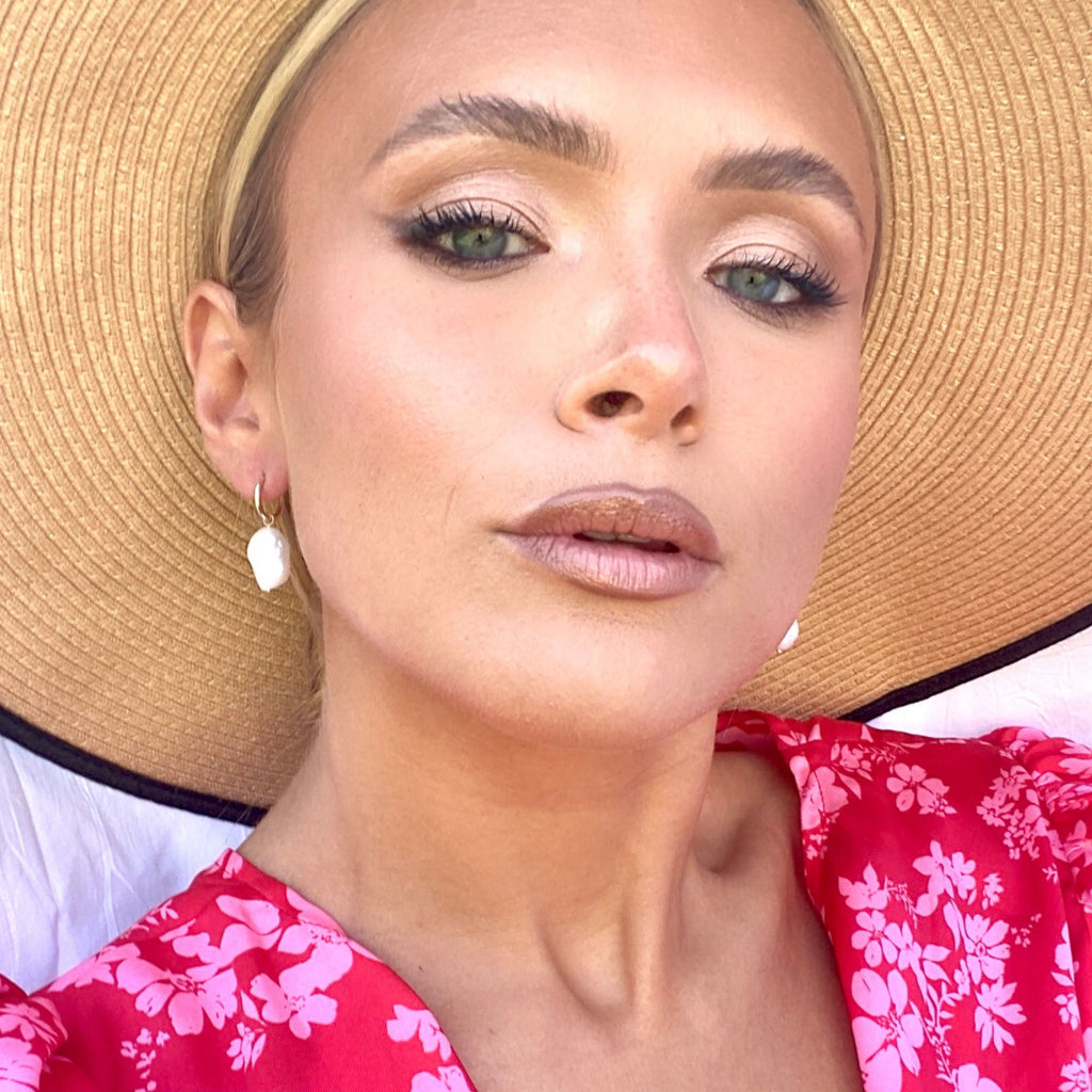 A blonde woman wearing a straw hat and gold huggie earrings with baroque pearl charms by Misia Mae