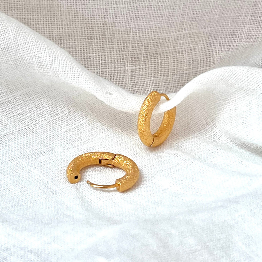 small chunky gold hoop earrings on a white linen fabric