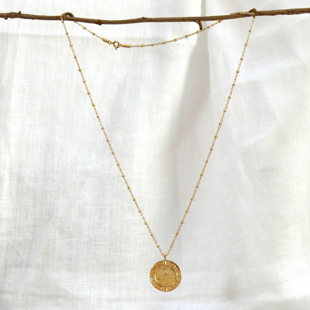 Gold pendant necklace by Misia Mae on a white linen background
