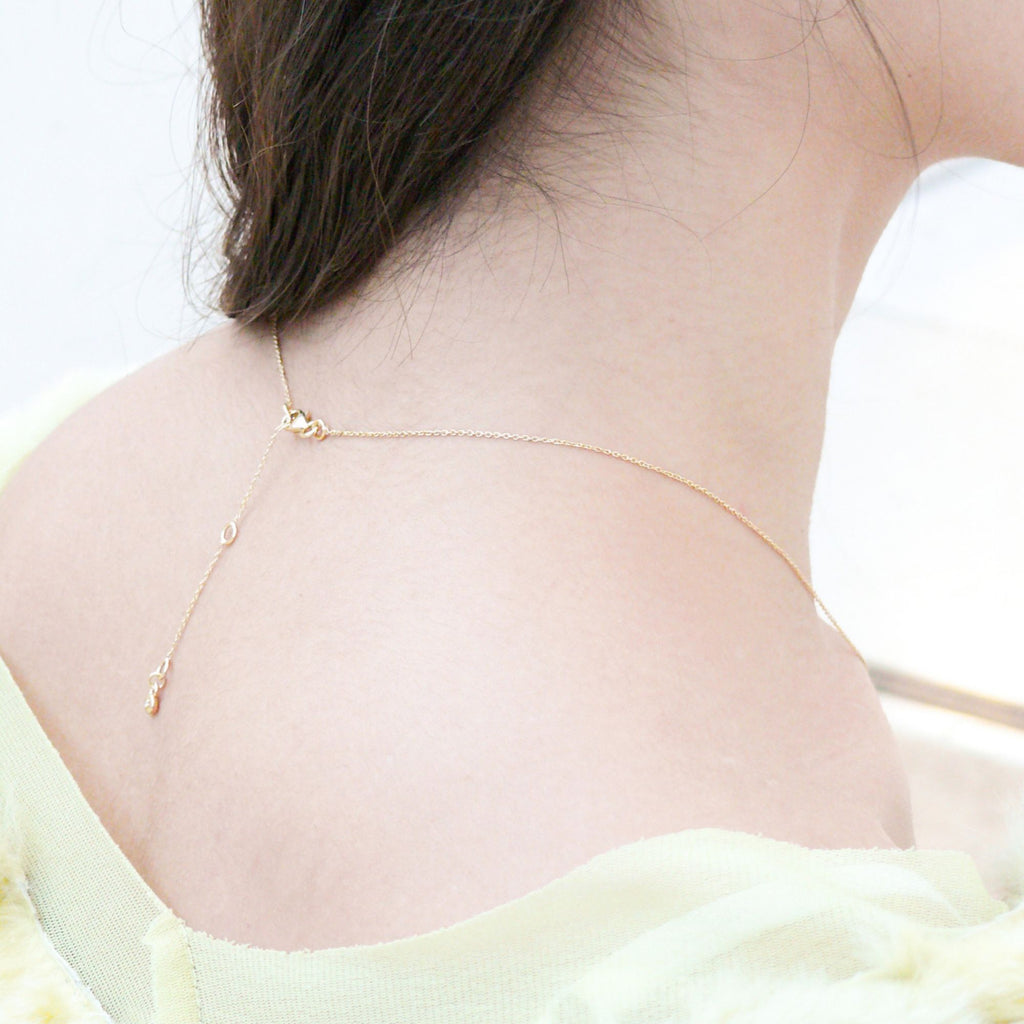 A brunette woman showing her back and adjustable lengths of the heart gold necklace by Misia Mae