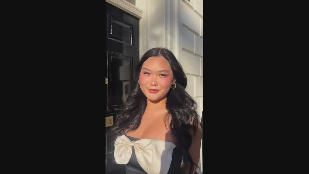 a brunette woman wearing a low neck black silk dress with a white bow, and pearl hoop earrings from the Sophie collection by Misia Mae