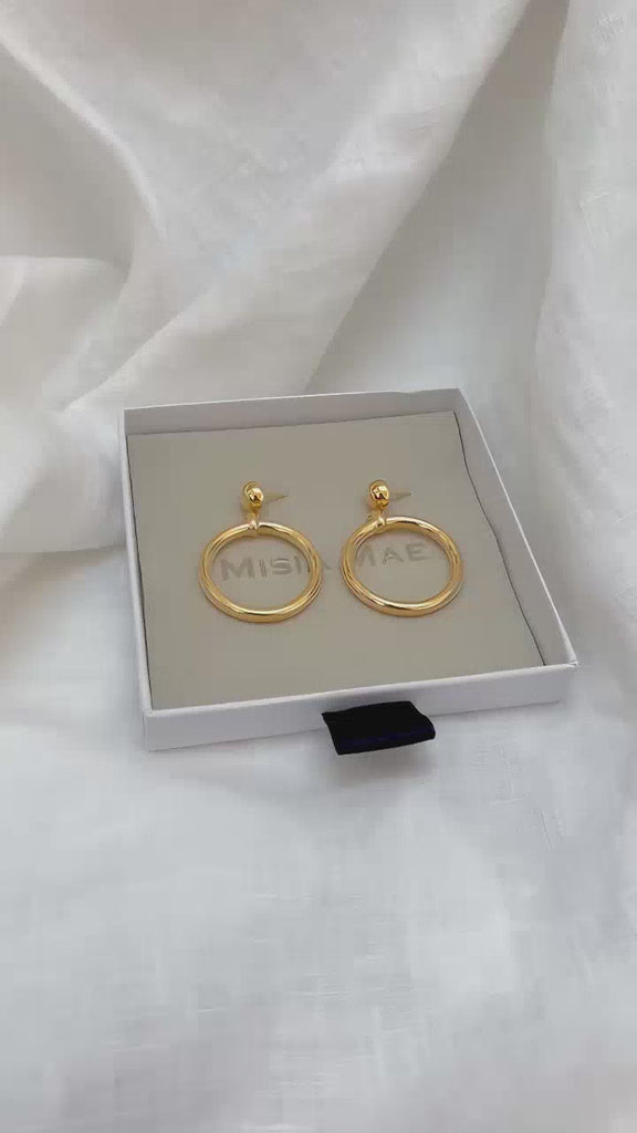 chunky gold earrings from the Audrey collection by Misia Mae. The earrings are in the box, and then are modelled by a dark haired woman