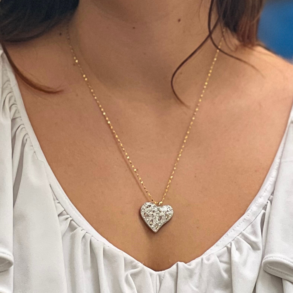 A dark haired woman wearing a white top and silver heart necklace by Misia Mae