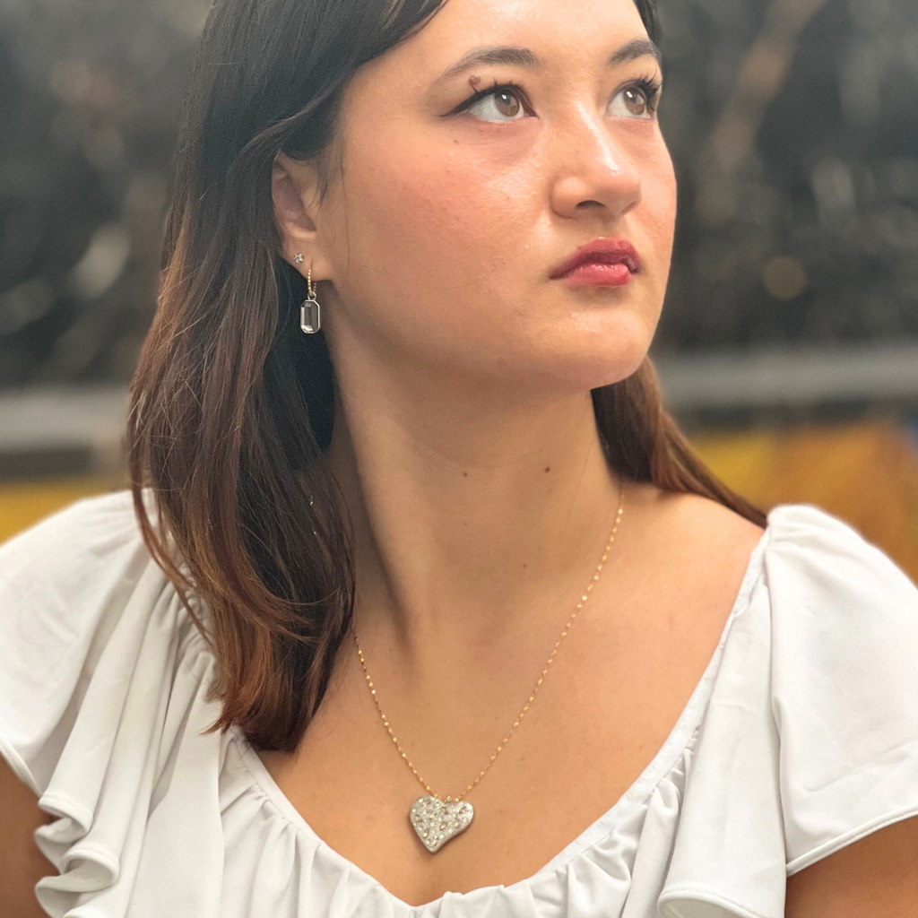 A dark haired woman waring a white top and silver heart necklace with zirconias