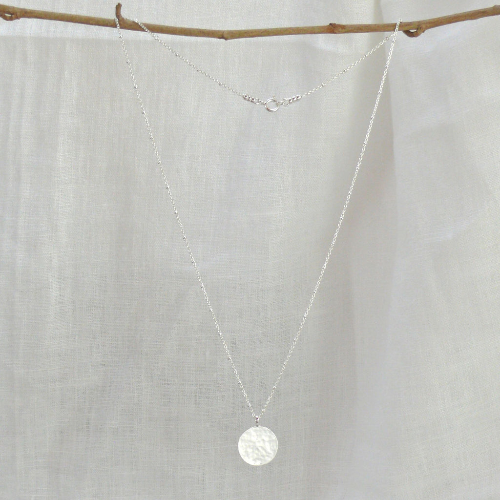 Silver pendant necklace on a white linen background. The necklace by Misia Mae