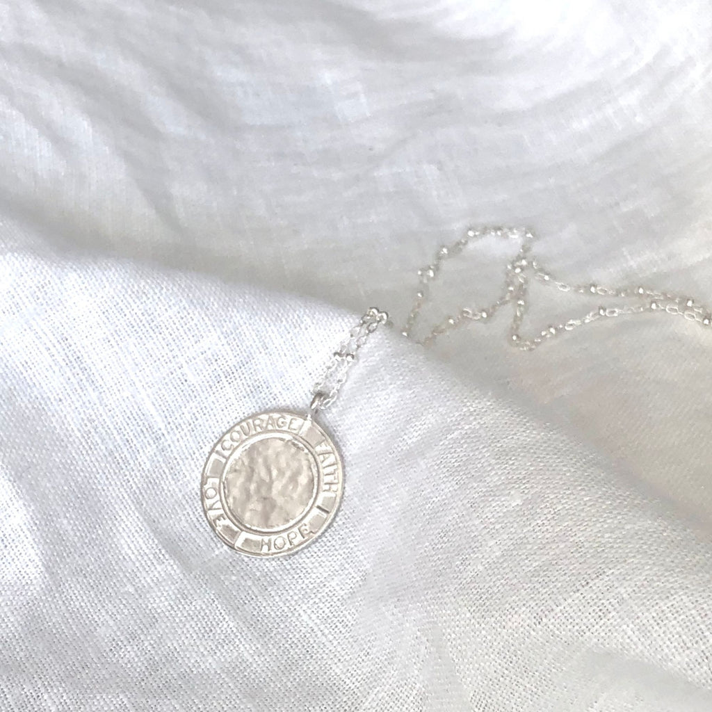 silver satellite necklace from the Courage collection by Misia Mae placed  on a white linen cloth
