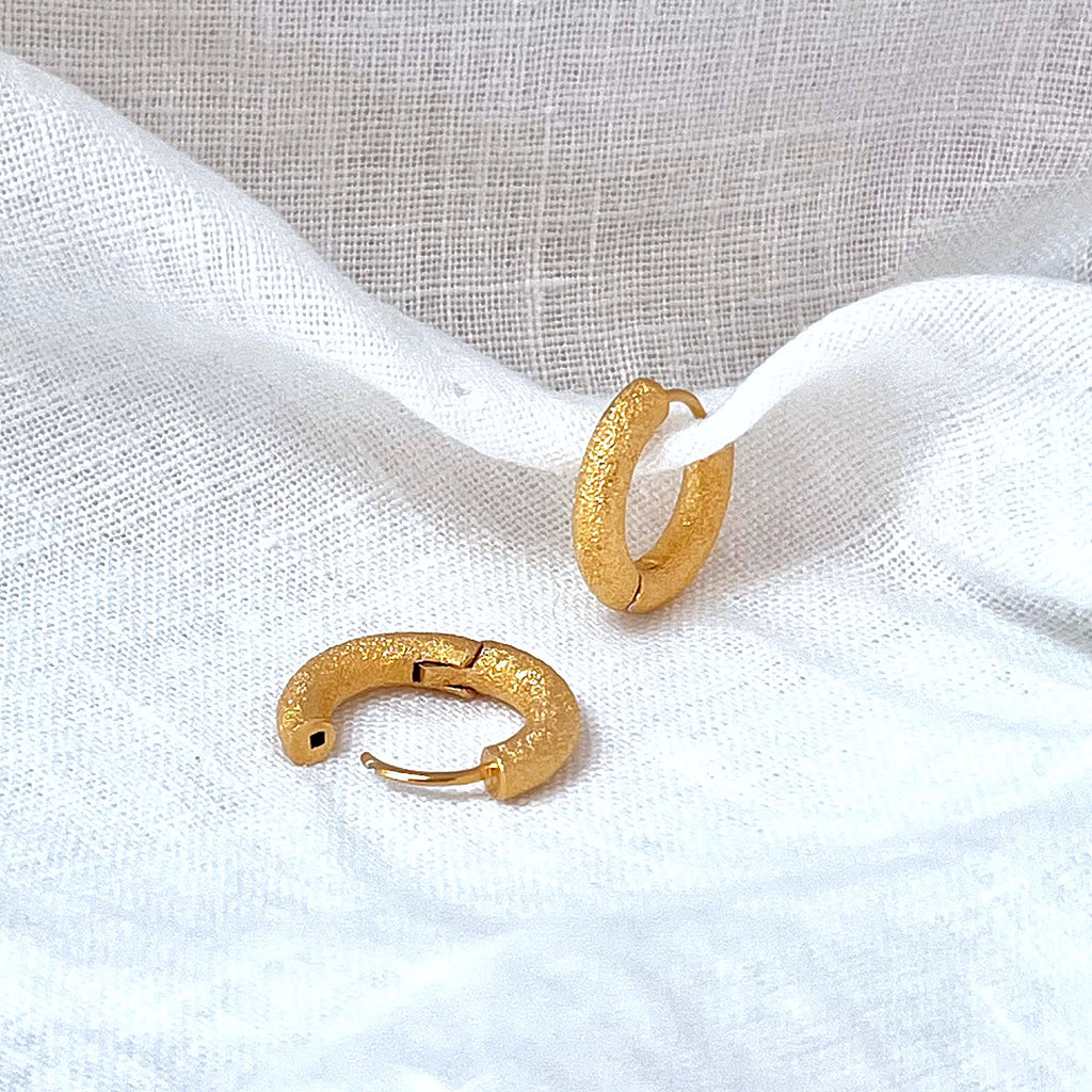 Chunky gold earringsby Misia Mae on a white linen background