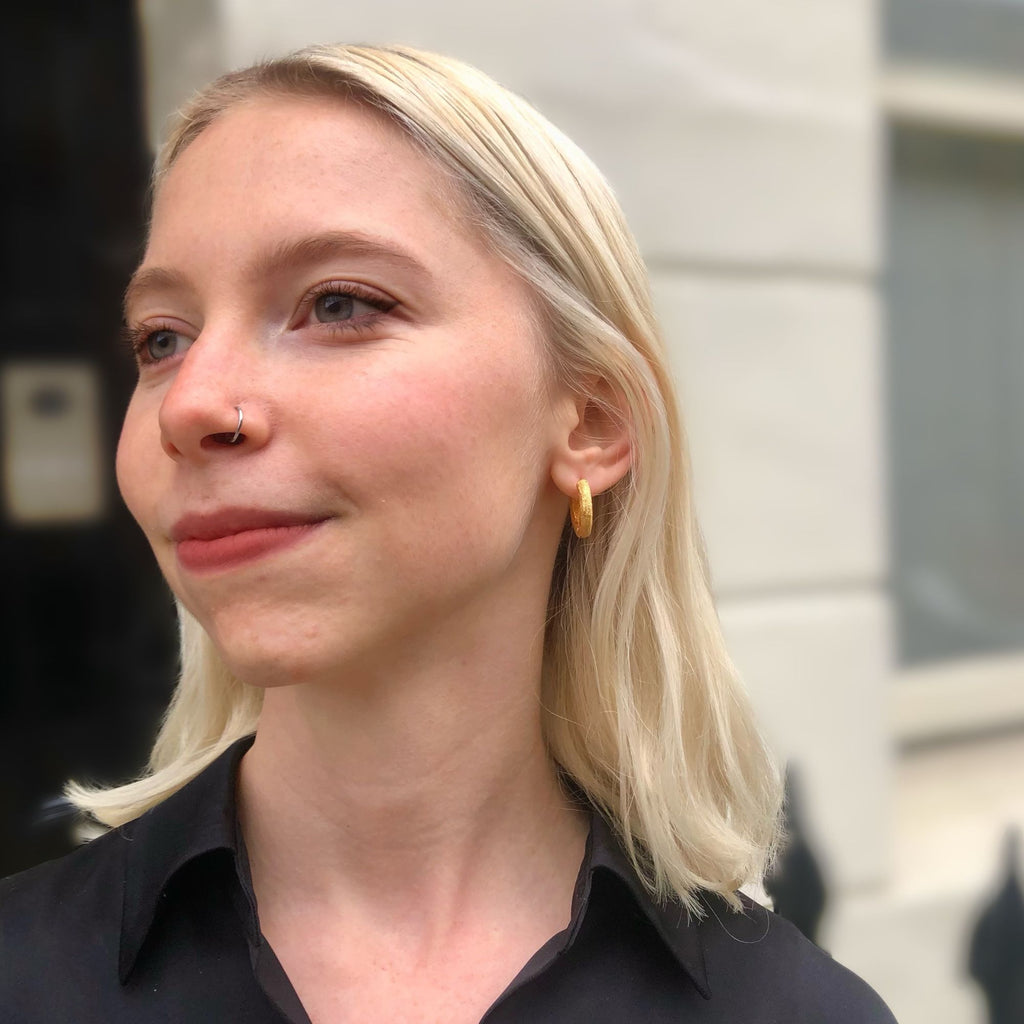 A blonde woman wearing textured gold hoop earrings by Misia Mae