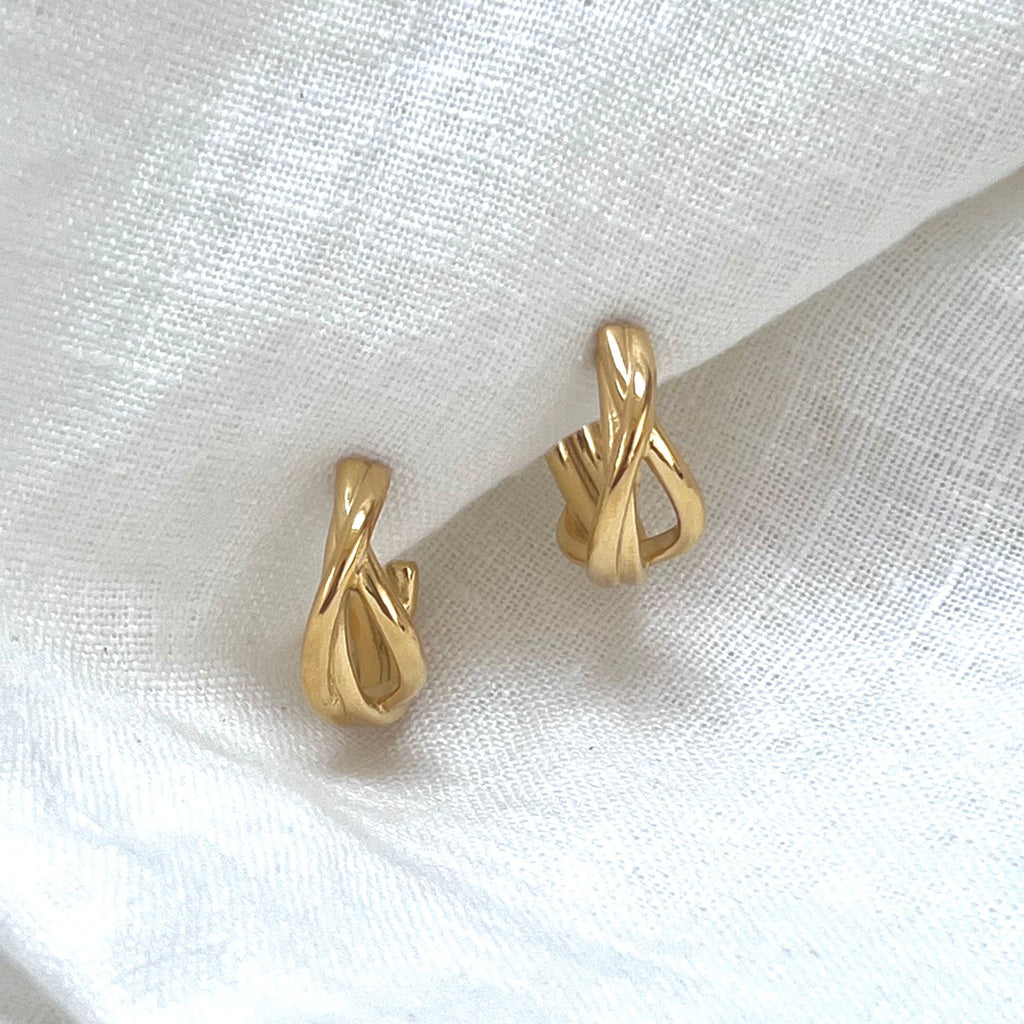 Gold twisted hoop earrings on a white linen fabric. Earrings by Misia Mae