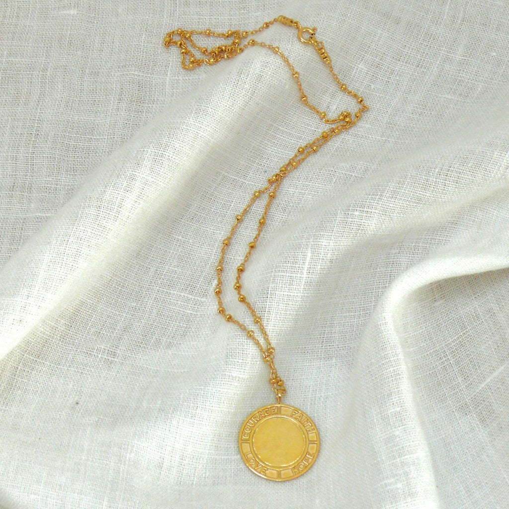 Gold courage necklace by Misia Mae on a white linen fabric