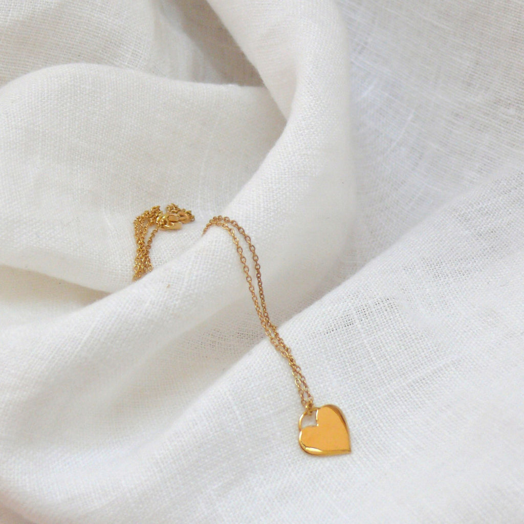 Heart gold necklace from the Daisy collection by Misia Mae. The necklace is on a white linen background.