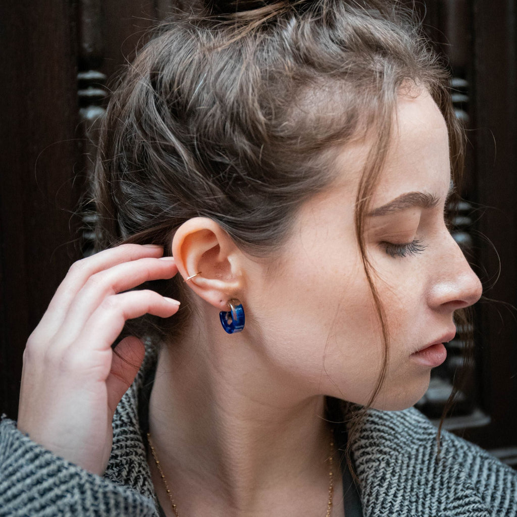 A dark blonde woman wearing a herringbone coat and blue tortoiseshell earrings by Misia Mae